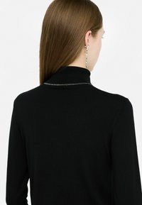 Zwarte coltrui met een geribbelde textuur en subtiele metallic draaddetails langs de kraag. Beschikt over lange mouwen.