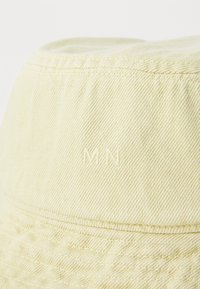 Cappello a secchiello giallo in denim con superficie testurizzata. Presenta bande cucite e le lettere "MN" ricamate sul lato.