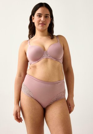 Kvinde med mellemtonet hud og mørkt hår iført matchende mauve bh og trusser med høj talje og blonder, står foran en ensfarvet lys baggrund.