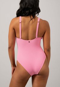 Roze badpak met dunne verstelbare bandjes, gestructureerde stof en een metalen accent op de rug. Volledige dekking ontwerp.