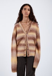 Stickad cardigan med horisontella ränder i varma nyanser av beige, brunt och gult, med v-ringning, långa ärmar och knäppning fram.