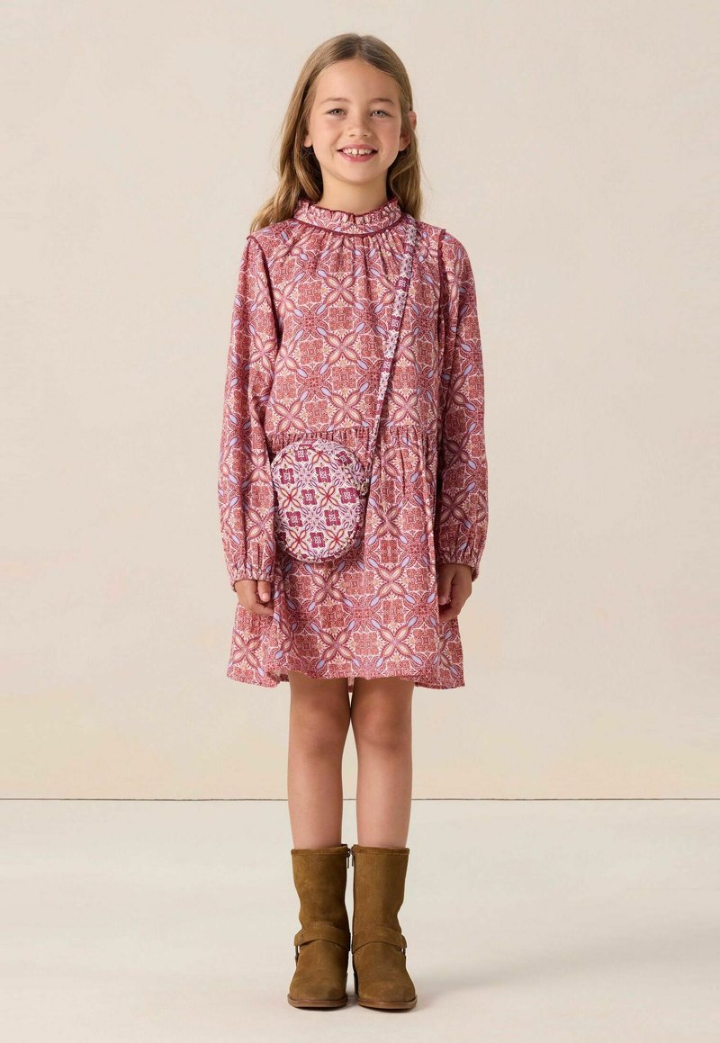 Rosa gemustertes Kleid mit langen Ärmeln, Rüschenausschnitt und einem ausgestellten Rock. Braune Stiefeletten und eine kleine passende Umhängetasche.