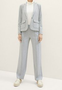 Lichtgrijs op maat gemaakt pak met een getailleerde blazer en wijde pijpen, vervaardigd uit zacht materiaal. Bevat twee voorzakken en contrasterende stiksels.