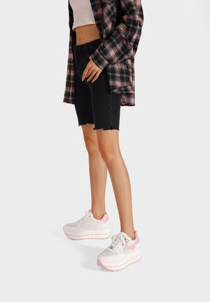 Sneakers bianchi e rosa chiaro con una suola spessa e stratificata, realizzati con materiali a rete e lisci. Il design include un accento rosa sul lato.