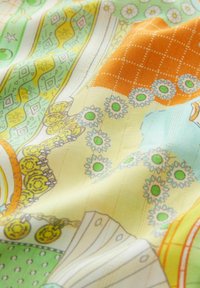 Mintás szövet, mely zöld, sárga, narancs és kék színeket tartalmaz, virágos és geometrikus mintákkal, sima felülettel és aprólékos részletekkel.