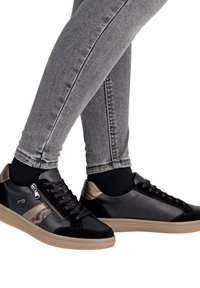 Baskets en cuir noir et en daim avec des accents dorés et des détails zippés, associées à un jean gris ajusté, mettant en avant un design moderne et épuré.