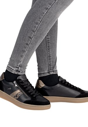 Baskets en cuir noir et en daim avec des accents dorés et des détails zippés, associées à un jean gris ajusté, mettant en avant un design moderne et épuré.