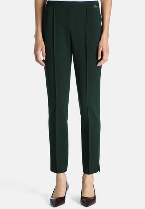 Pantalon droit vert foncé avec une fente latérale près de la cheville, porté avec des escarpins à bouts pointus et texture foncée.