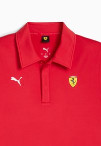 Simára sima anyagból készült piros póló. Hajlított gallérral, három gombos nyakrésszel és fehér Puma logóval rendelkezik. Hímzett Ferrari emblémát is tartalmaz.