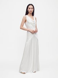 Woman with long dark hair wearing a sleeveless white satin gown standing against a plain white background.