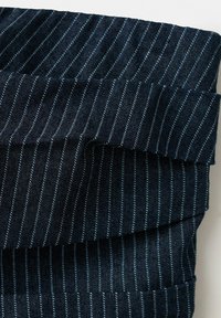 Tissu bleu foncé avec de fines rayures blanches verticales plié soigneusement sur une surface blanche.