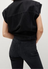 Top de denim negro con mangas cortas, combinado con jeans negros de talle alto que cuentan con bolsillos traseros y detalles de costura en contraste.