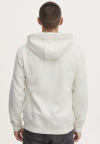 Hvit hettegenser med snøring i hetta, ribbede mansjetter og nederkant, med en glatt tekstur og minimalistisk design. Sett fra baksiden.