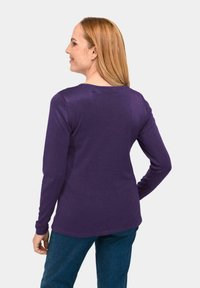 Paarse langemouwshirt met een ronde halslijn, geribbelde textuur en een licht gebogen zoom. Gepaard met donkerblauwe jeans, gezien vanaf de achterkant.