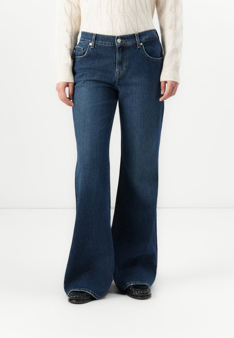 Dark blue flared jeans crafted from denim, featuring two front pockets, a zip fly with button, and stitched seams along the legs.