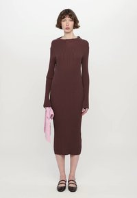 Rochie midi maro cu dungi, cu mâneci lungi, design minimalist și accente laterale. Țesătură roz în mână, pantofi negri cu toc plat și barete.