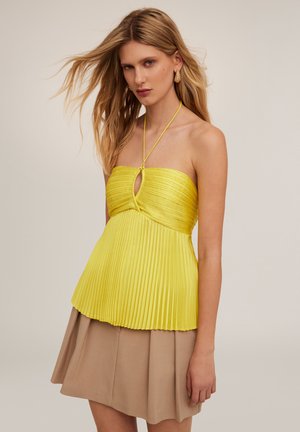 Top giallo a halter con dettaglio a chiave sul busto, abbinato a una gonna beige plissettata. Tessuto liscio, contrasto di colori vivaci.