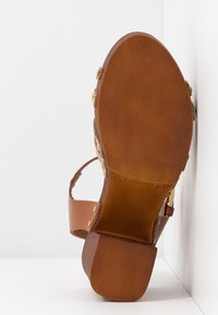 Sandale en cuir marron avec talon bloc en bois et bride réglable, semelle tournée vers l'avant sur fond blanc.