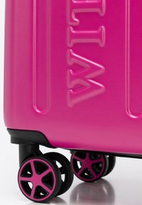 Valigia rigida di colore rosa intenso con finitura testurizzata, dotata di cinque ruote nere con raggi e logo del marchio impresso.