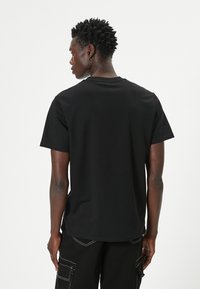 Camiseta de algodón negra de mangas cortas, con escote redondo y una textura suave, vista desde la parte de atrás. Presenta un ajuste holgado y sin gráficos.