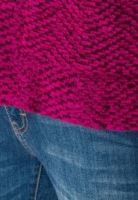 Chundelatý magentový svetr s texturovaným vzorem, kombinovaný s modrými denimovými džíny. Svetr má tkaný vzhled a měkký pocit.