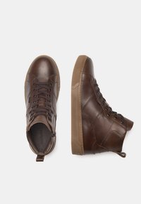 Sneakers alti in pelle marrone con superficie texture, punta rotonda e suola in gomma. Dotati di lacci e di un anello sul tallone per una facile calzata.