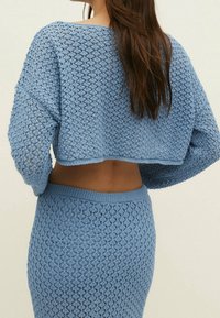 Haut en crochet bleu clair et jupe assortie, présentant un design à maille ouverte avec un motif losange texturé et un col ainsi qu'une ceinture côtelés.