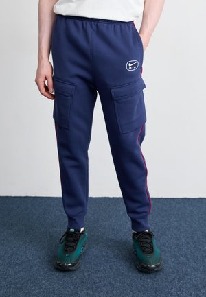 Tumesinine kaubasweatpants kahe esipocketiga, punaste külgtriipudega ja väikese valge Nike Air logoga. Pehme kangas ja elastne vöökoht.