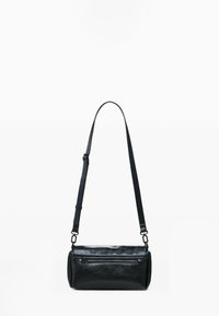 Sac en cuir noir en forme de cylindre avec une poche zippée à l'avant et une bandoulière réglable, sur fond blanc.
