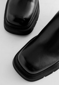 Bottines en cuir noir à bout carré, dotées d'une semelle en caoutchouc noir épaisse et d'une finition lisse et réfléchissante.