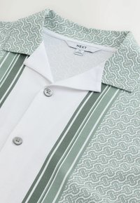 Close-up of a green and white shirt with a patterned collar and vertical stripes, showing front buttons and the brand label "NEXT" size medium.