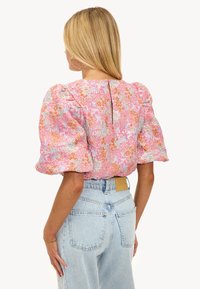 Blouse florale avec des manches bouffantes dans des tons de rose, orange et bleu. Tissu texturé avec un dos en fente. Portée avec un jean taille haute bleu clair.