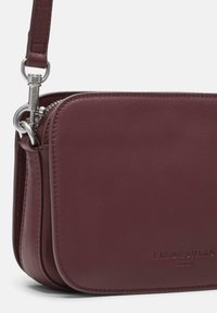 Bordowa skórzana torebka na ramię z zamkiem błyskawicznym, srebrnymi elementami i wytłoczonym logo. Gładka faktura z zaokrąglonymi krawędziami.