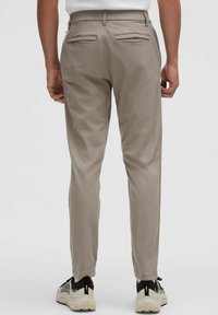 Beżowe, dopasowane spodnie o wąskim kroju, z dwoma tylnymi kieszeniami i gładką fakturą tkaniny, zestawione z czarno-białymi butami sportowymi.