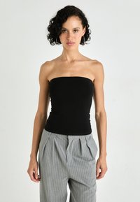 Top nero senza spalline realizzato in tessuto elasticizzato, design aderente, abbinato a pantaloni grigi a righe sottili a vita alta per un look contemporaneo.
