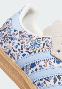Blaue Sneakers mit floralem Muster, die helle blaue Akzente, Wildlederelemente und eine Gummisohle haben. Goldenes "SAMBA"-Branding vorhanden.