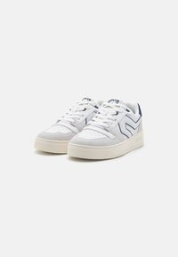 Vita sneakers med grå mockadetaljer, snörningsdesign, vadderad krage och blå logotyp. Lätt upphöjd gummisula med texturerat mönster.