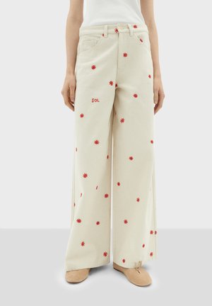 Pantaloni a gamba larga in cotone crema con ricami floreali rossi e testo "SOL." Presentano tasche frontali e una vestibilità rilassata.