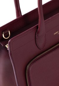 Burgundy leather handbag with a textured finish, featuring gold hardware, dual handles, and a zippered exterior pocket.