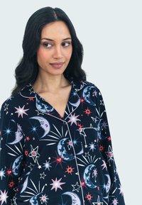 Marine blauwe pyjama set met maan- en sterrenpatronen in rood en wit, voorzien van een notch kraag, een voorzak en contrasterende witte piping.