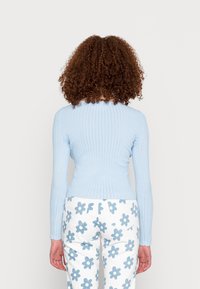 Camisola de manga longa em azul claro com um design ajustado, combinada com calças brancas com um padrão de flores azuis. Tecido texturizado com decote redondo.