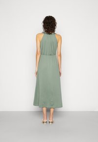 Vestido maxi verde, sem mangas, com cintura franzida, textura suave e silhueta fluida. Vista de trás, combinado com saltos abertos.