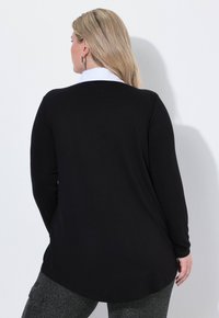 Czarny longsleeve z okrągłym dołem i białym kołnierzykiem, wykonany z miękkiego materiału, prezentowany z tyłu.