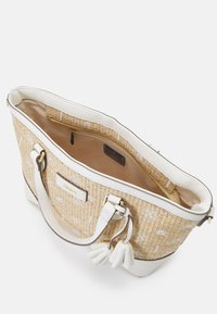 Sac fourre-tout en paille tissée avec des accents en cuir blanc, une poche zippée à l'intérieur, une doublure beige clair et des pompons décoratifs sur les poignées.
