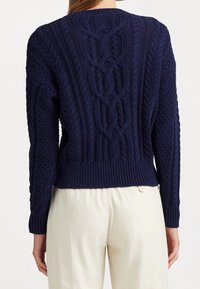 Pull en maille bleu marine avec motifs torsadés et ourlet côtelé. Présente un tissu texturé et un col rond, porté avec un pantalon de couleur claire.