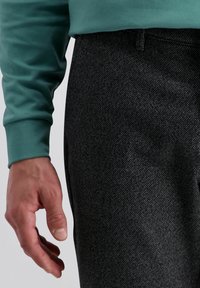 Sweatshirt vert avec un col rond et des poignets ajustés, associé à un pantalon sombre texturé affichant un subtil motif en chevrons.
