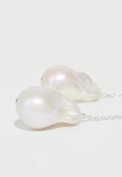 Baltos gėlavandenės perlų auskarai su netaisyklingomis organinėmis formomis, pritvirtinti plona sidabro grandinėlę. Lygi, blizgi paviršius su subtiliu blizgesiu.