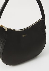 Black leather handbag with a curved shape, gold zipper detail, and embossed brand logo. Smooth texture with a single shoulder strap.