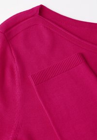 Fuksia neulepaita pyöreällä pääntiellä ja pienellä taskulla edessä, jossa on resoritettuja yksityiskohtia ja sileä pinta.