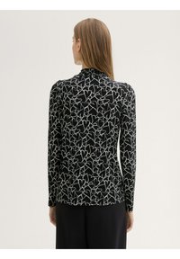 Zwarte blouse met lange mouwen en een wit hartpatroon. Heeft een gathered halslijn en een zachte stof. Moderne pasvorm met een rechte snit aan de onderkant.